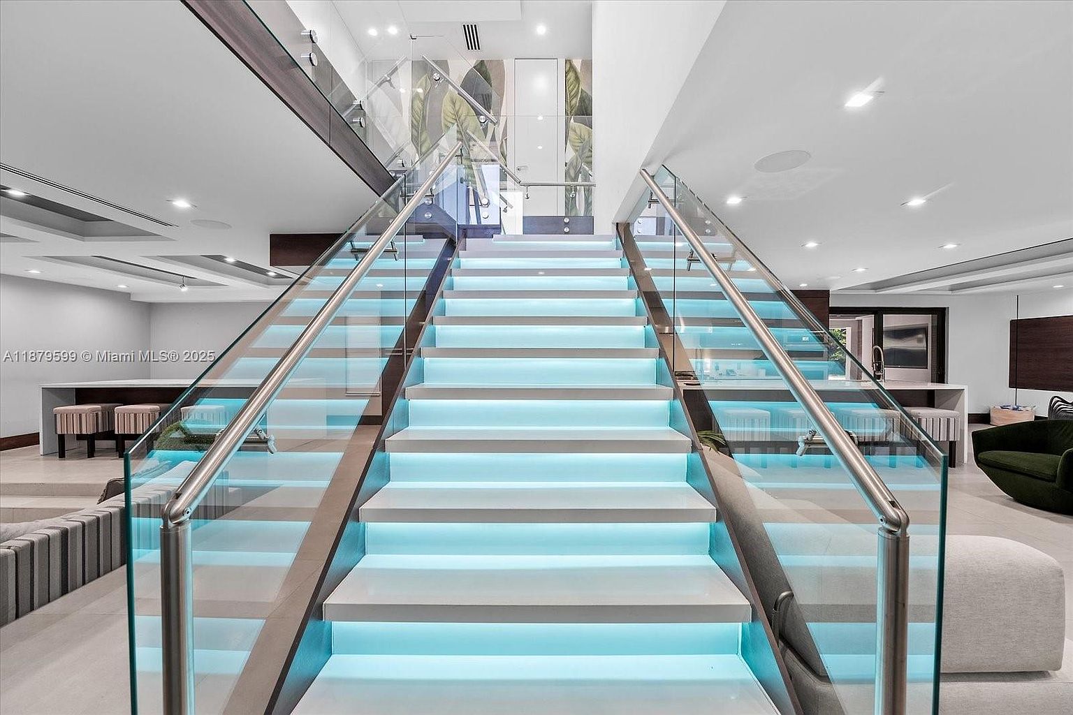 This interior shot showcases a modern staircase with illuminated steps, glass railings, and stainless steel handrails. The design is sleek and contemporary, creating a bright and inviting transition between floors. The surrounding space features neutral tones and recessed lighting, enhancing the overall elegance.