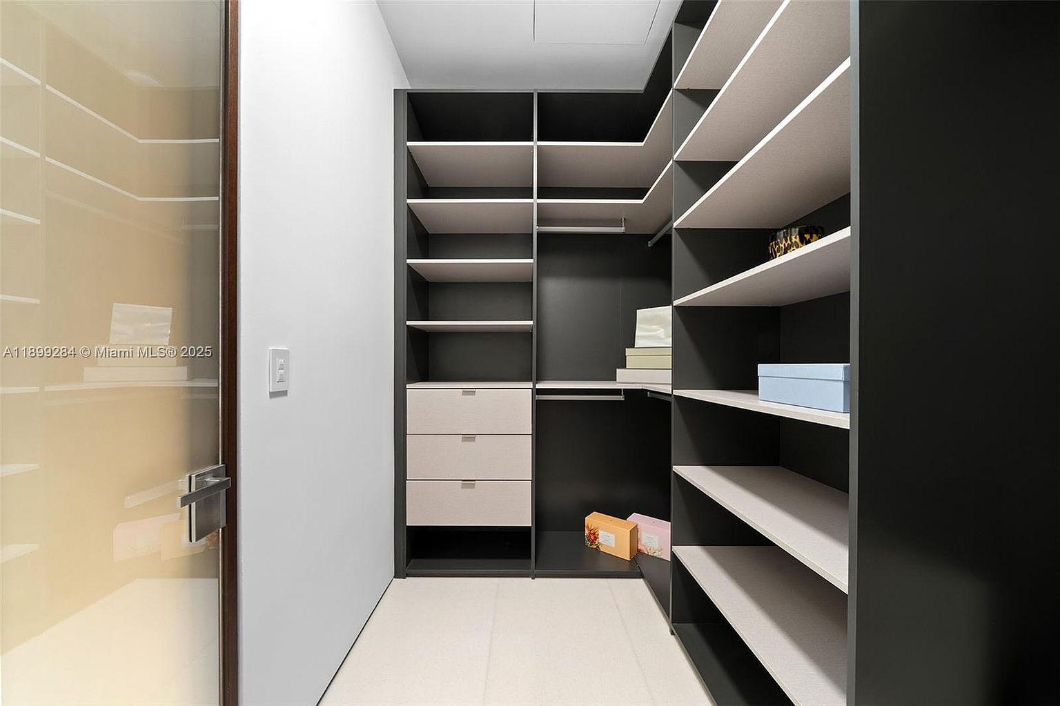 This is a well-organized walk-in closet featuring a dark gray shelving system with light-colored shelves and drawers. The closet includes both open shelving and hanging rods, providing ample storage space. The overall impression is clean, modern, and functional, ideal for showcasing storage solutions in a real estate listing.