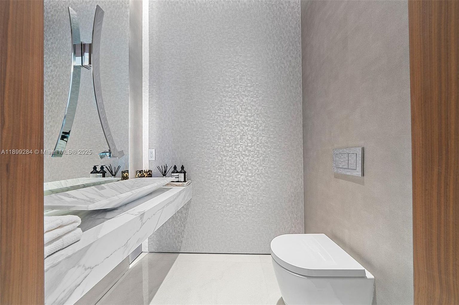 This is a modern bathroom featuring a unique marble countertop with an integrated sink and a stylish, curved faucet. The walls are adorned with textured wallpaper, and a sleek, wall-mounted toilet adds to the contemporary aesthetic. The space is well-lit and appears clean and luxurious, perfect for a guest bathroom.