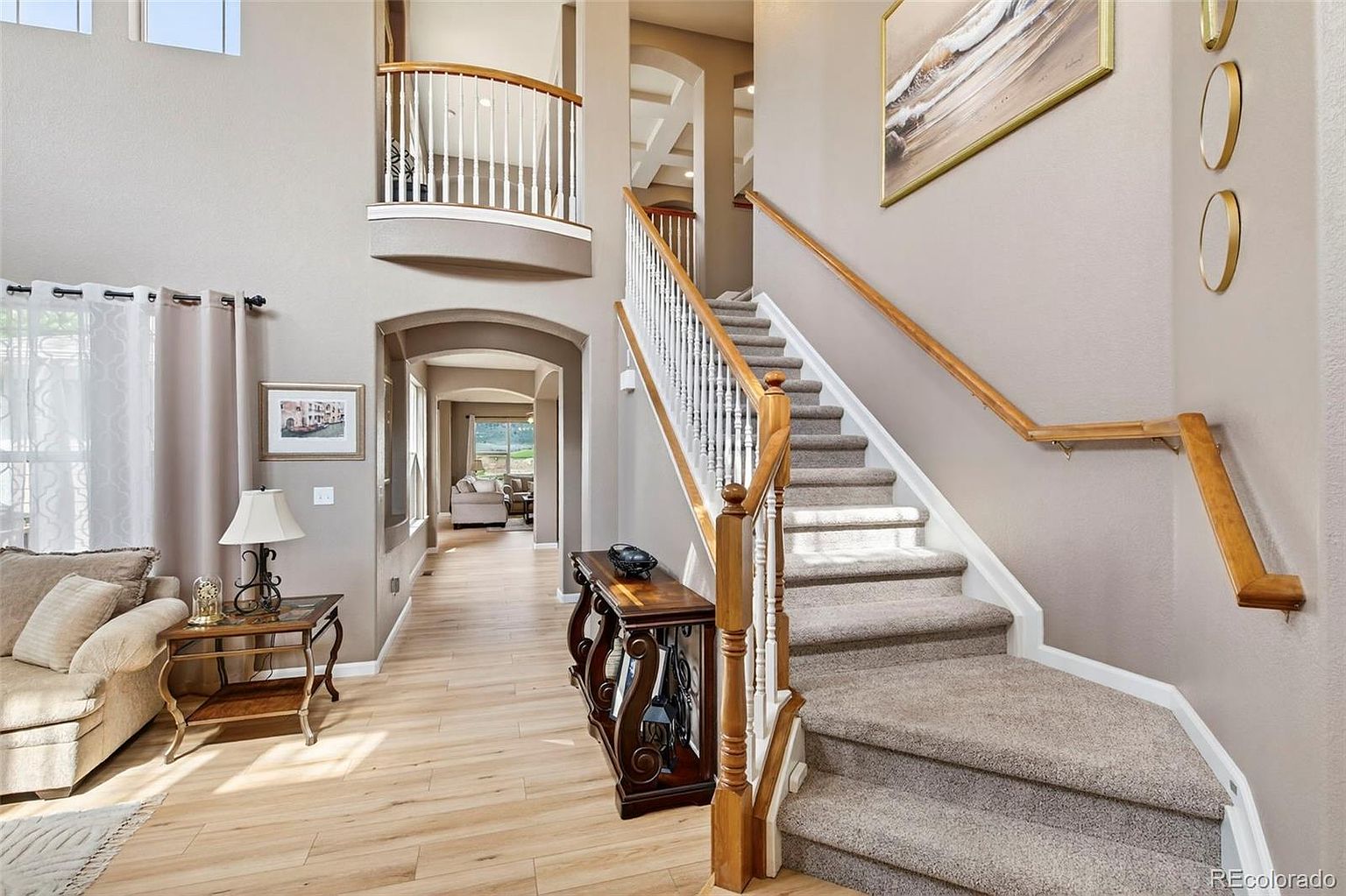 This interior shot showcases a grand hallway with a staircase leading to the upper level. The staircase features carpeted steps, a white balustrade, and a wooden handrail. The hallway is decorated with neutral-toned walls, wooden flooring, and elegant furniture, creating a welcoming and sophisticated atmosphere.