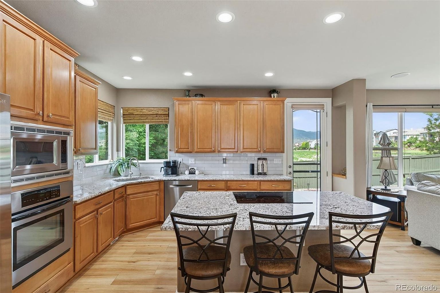 This is a well-lit kitchen featuring wooden cabinets, granite countertops, and stainless steel appliances. A central island with bar seating provides a focal point, while a window offers a view of the outdoors. The kitchen has a warm and inviting feel, perfect for cooking and entertaining.