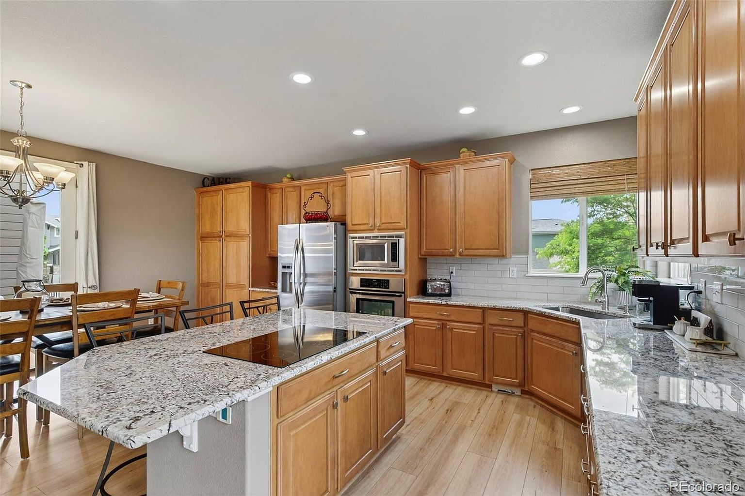 This is a well-lit kitchen featuring wooden cabinets, stainless steel appliances, and a large island with a granite countertop. The kitchen also has a dining area with a wooden table and chairs. The overall impression is a warm and inviting space, perfect for cooking and entertaining.