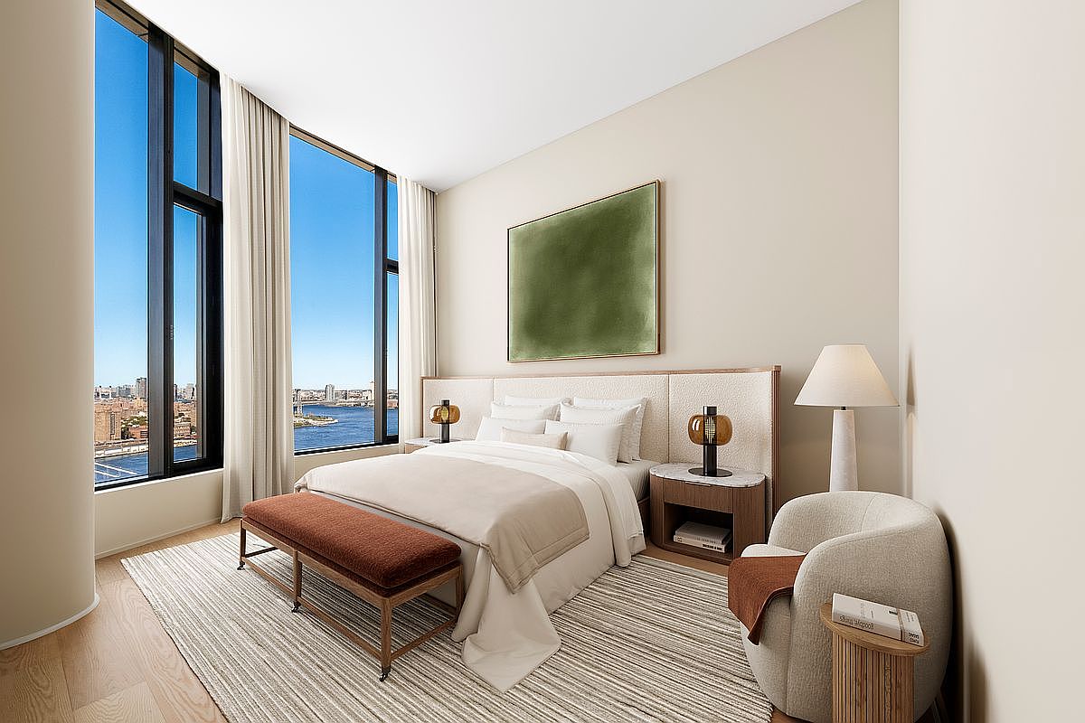 This sophisticated primary bedroom features a neutral color palette, floor-to-ceiling windows with expansive water views, and a plush, textured headboard. The room is furnished with a modern bed, a rich rust-colored bench, and a cozy armchair, creating a serene and luxurious atmosphere. The minimalist aesthetic is complemented by soft lighting and high-end finishes, making it an inviting retreat.