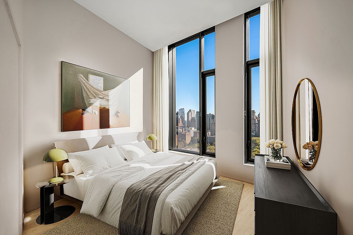 This modern, high-rise primary bedroom features floor-to-ceiling windows that offer a stunning, expansive view of the city skyline. The room is elegantly appointed with a neutral color palette, a plush bed with layered linens, and minimalist bedside tables with stylish green lamps. A sleek, dark wood dresser paired with an oval gold-framed mirror adds a touch of sophistication to the serene and airy space.