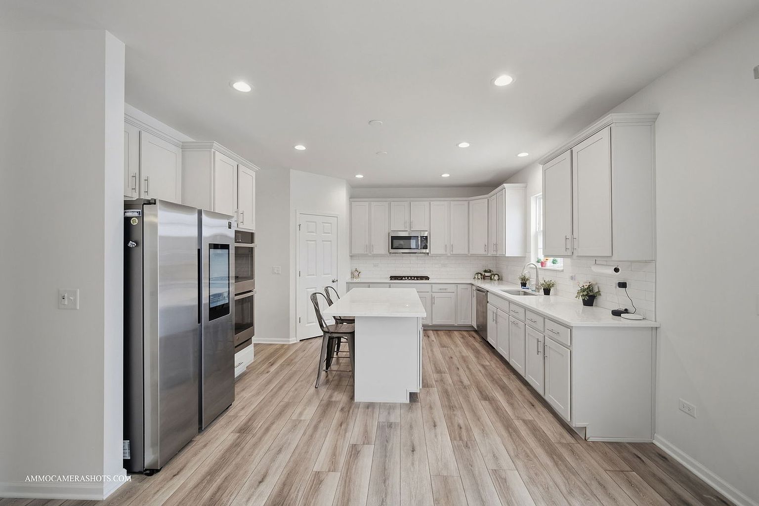 This is a bright and spacious kitchen featuring white cabinetry, stainless steel appliances, and light wood-look flooring. A central island provides additional counter space and seating, while recessed lighting illuminates the entire area. The kitchen has a clean and modern aesthetic, perfect for cooking and entertaining.
