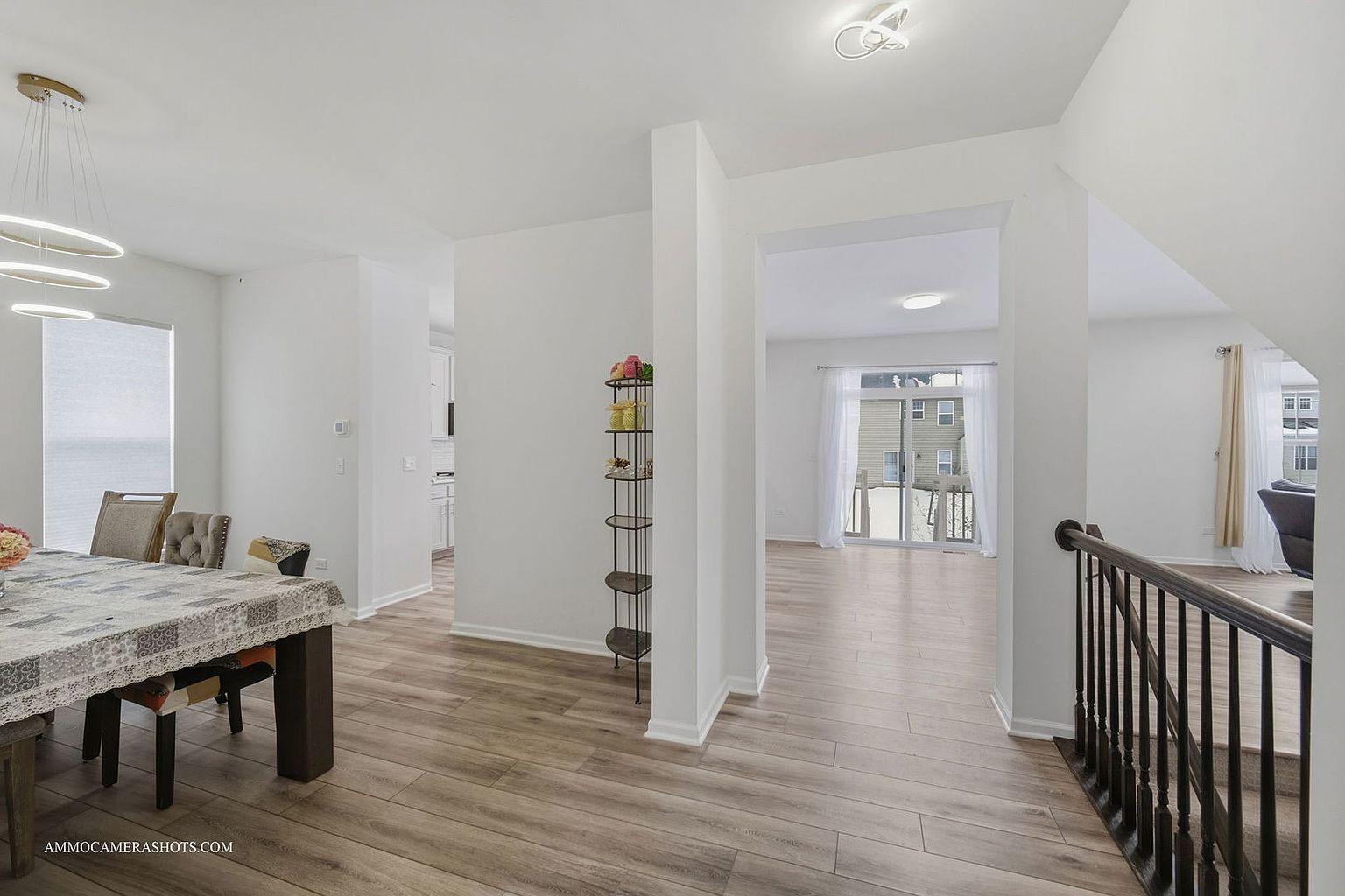 This interior shot showcases a hallway with wood-look flooring leading into a bright living space. A dining area is visible to the left, while a staircase with dark railings is on the right. The walls are painted in a neutral tone, creating a clean and airy atmosphere.