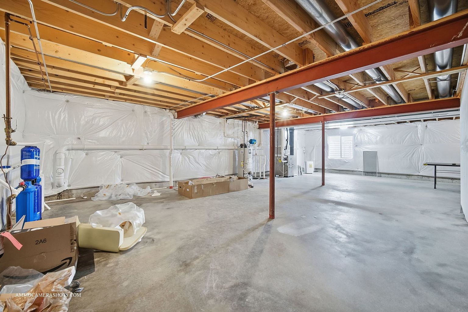 This is an unfinished basement with exposed wooden ceiling beams and ductwork. The walls are lined with white plastic sheeting, and the concrete floor is bare. The space is large and open, offering potential for customization and finishing to suit various needs.