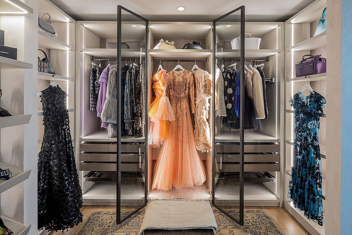 This is a well-organized walk-in closet featuring custom shelving and hanging rods. The closet is illuminated with integrated lighting, highlighting the clothing and accessories. The design incorporates glass doors and drawers, adding a touch of elegance and functionality to the space.