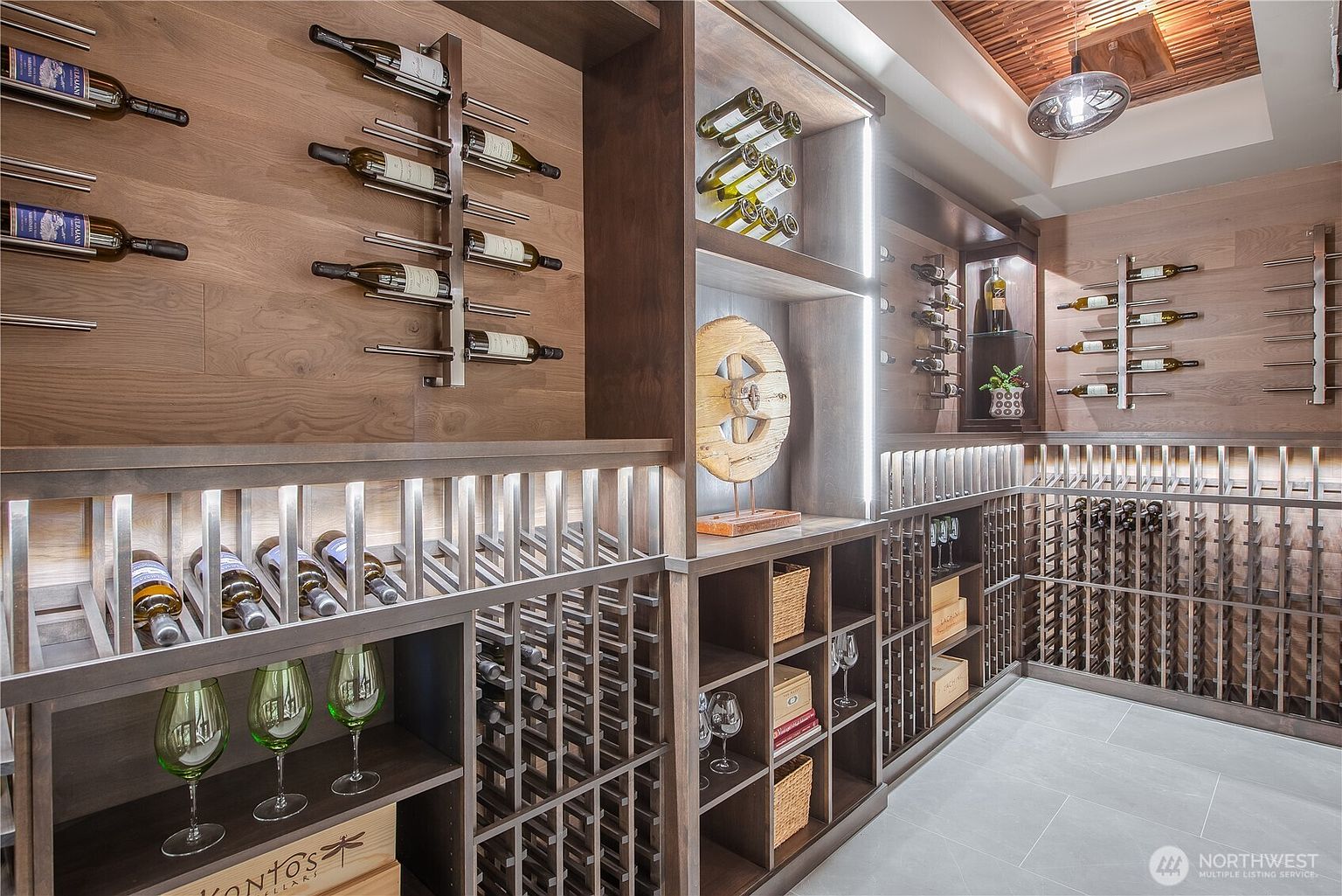 This is an interior shot of a well-appointed wine cellar. The cellar features custom wooden shelving and racks designed to hold numerous wine bottles, along with dedicated spaces for wine glasses and accessories. The lighting is strategically placed to highlight the collection, creating an elegant and sophisticated ambiance.