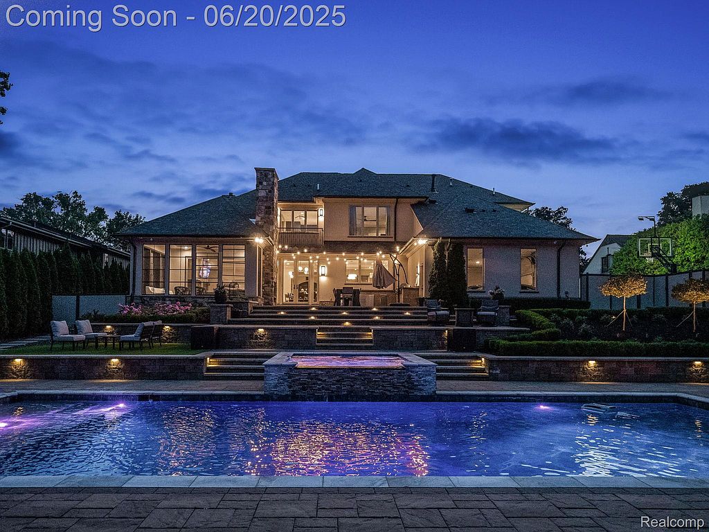 This image showcases the rear exterior of a luxurious home, highlighting a stunning pool and spa area. The multi-tiered landscaping leads up to the house, which features large windows and outdoor lighting, creating an inviting ambiance. The overall impression is one of high-end relaxation and entertainment.