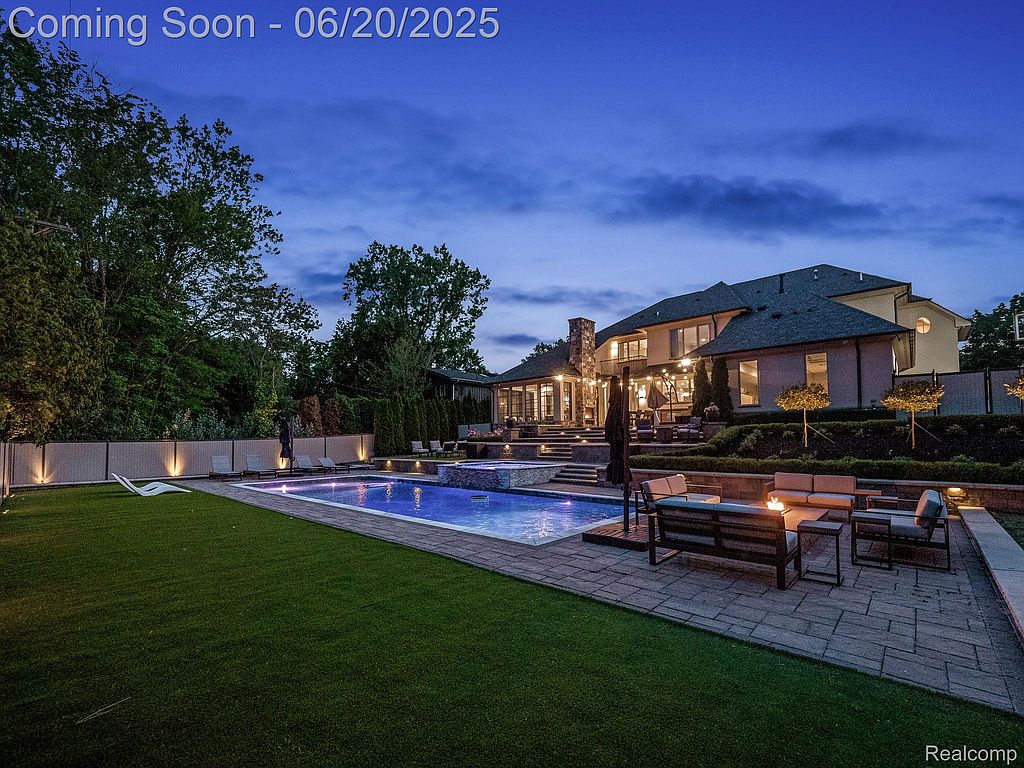 This image showcases a luxurious backyard featuring a large swimming pool and spa area. A well-manicured lawn and patio with outdoor seating surround the pool, creating an inviting space for relaxation and entertainment. The property includes a substantial house in the background, suggesting a high-end residential estate.