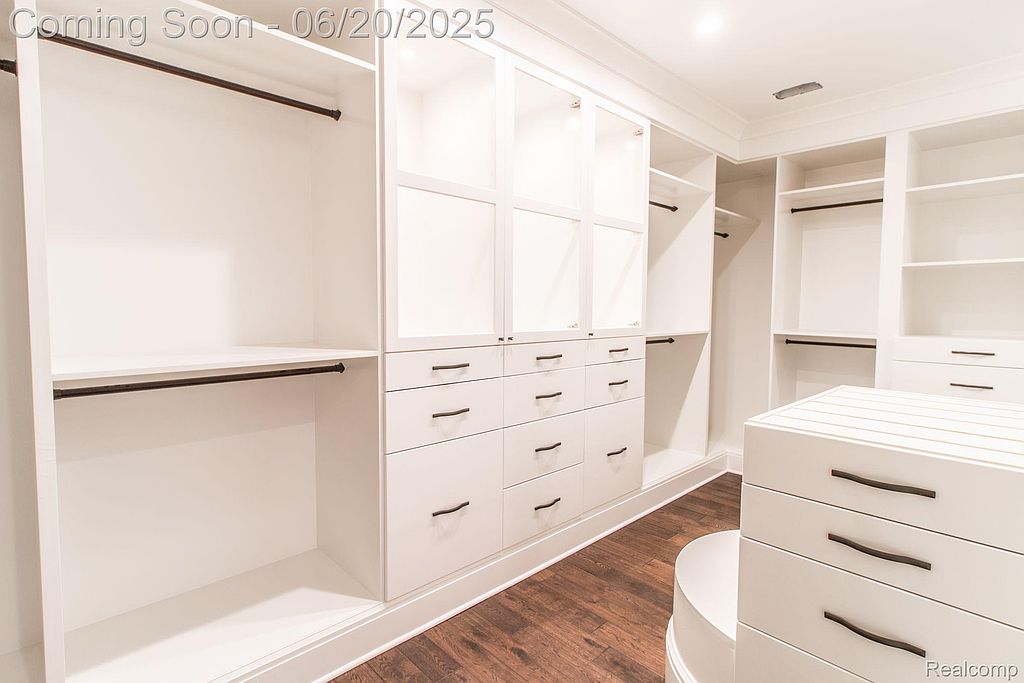 This is a spacious walk-in closet featuring custom white cabinetry with drawers, shelving, and hanging rods. The closet is well-lit and organized, offering ample storage space. The dark wood flooring adds a touch of elegance to the design.