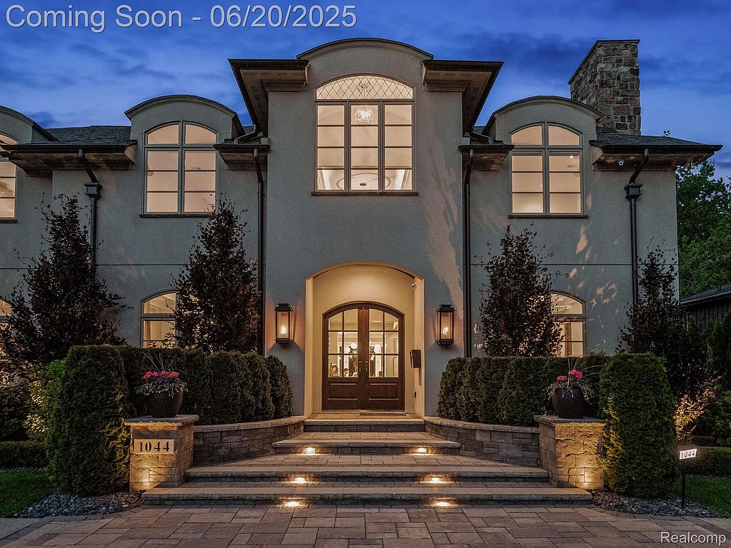 This is a stately front view of a luxurious home, featuring a symmetrical design with arched windows and a grand entrance. The well-manicured landscaping, stone accents, and illuminated steps create an inviting and elegant curb appeal. The property exudes sophistication and high-end living.