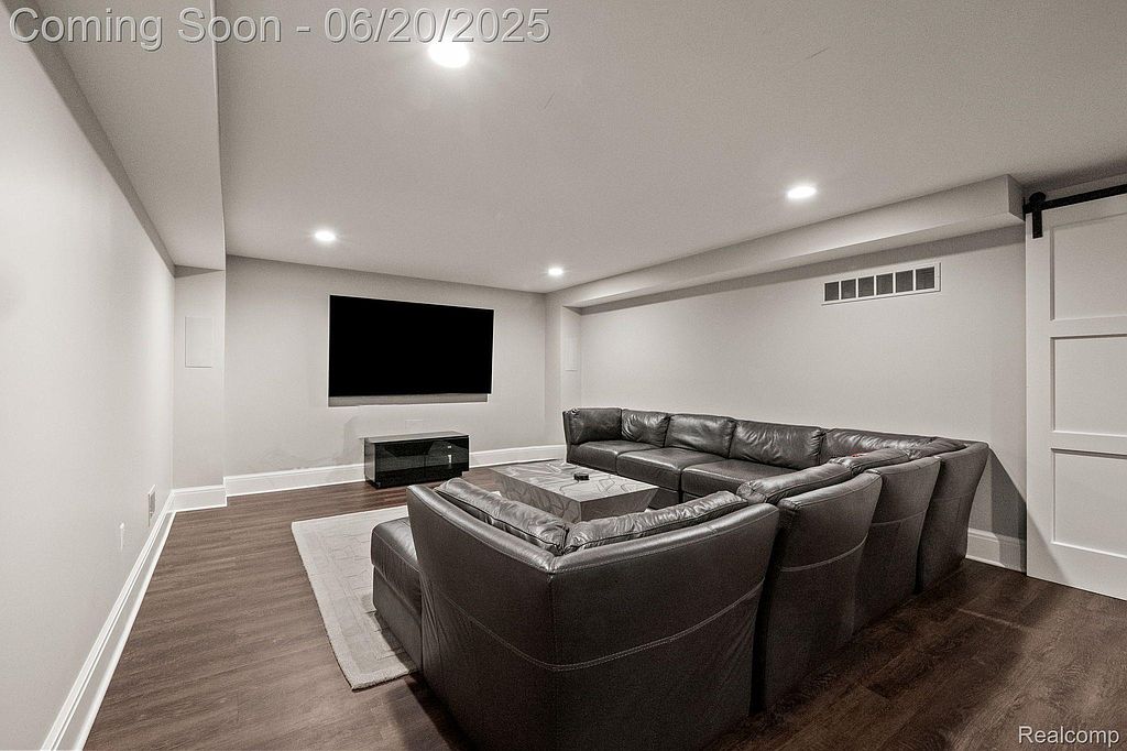 This is a finished basement featuring a large sectional sofa, a flat-screen TV, and modern recessed lighting. The dark wood flooring and neutral wall colors create a cozy and inviting atmosphere. The space is well-lit and appears to be designed for entertainment and relaxation.