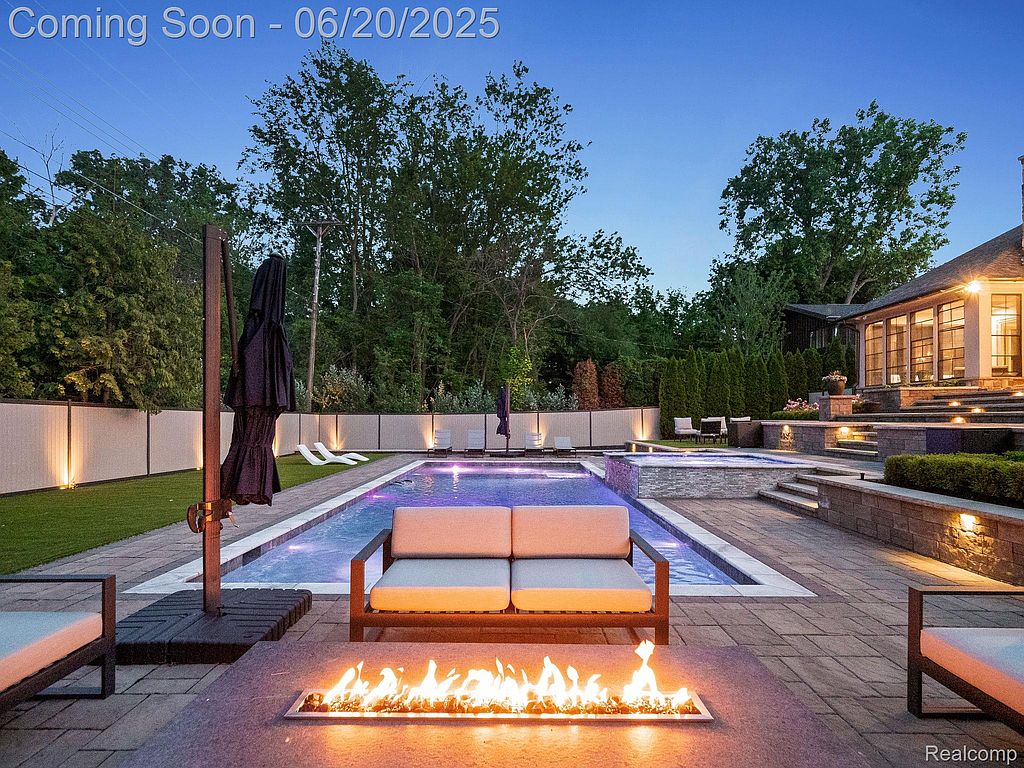 This image showcases a luxurious backyard pool and spa area, complete with modern outdoor furniture and a fire pit. The pool is surrounded by a well-maintained patio and landscaping, creating an inviting and relaxing atmosphere. The adjacent house features large windows, suggesting ample natural light and views from the interior.