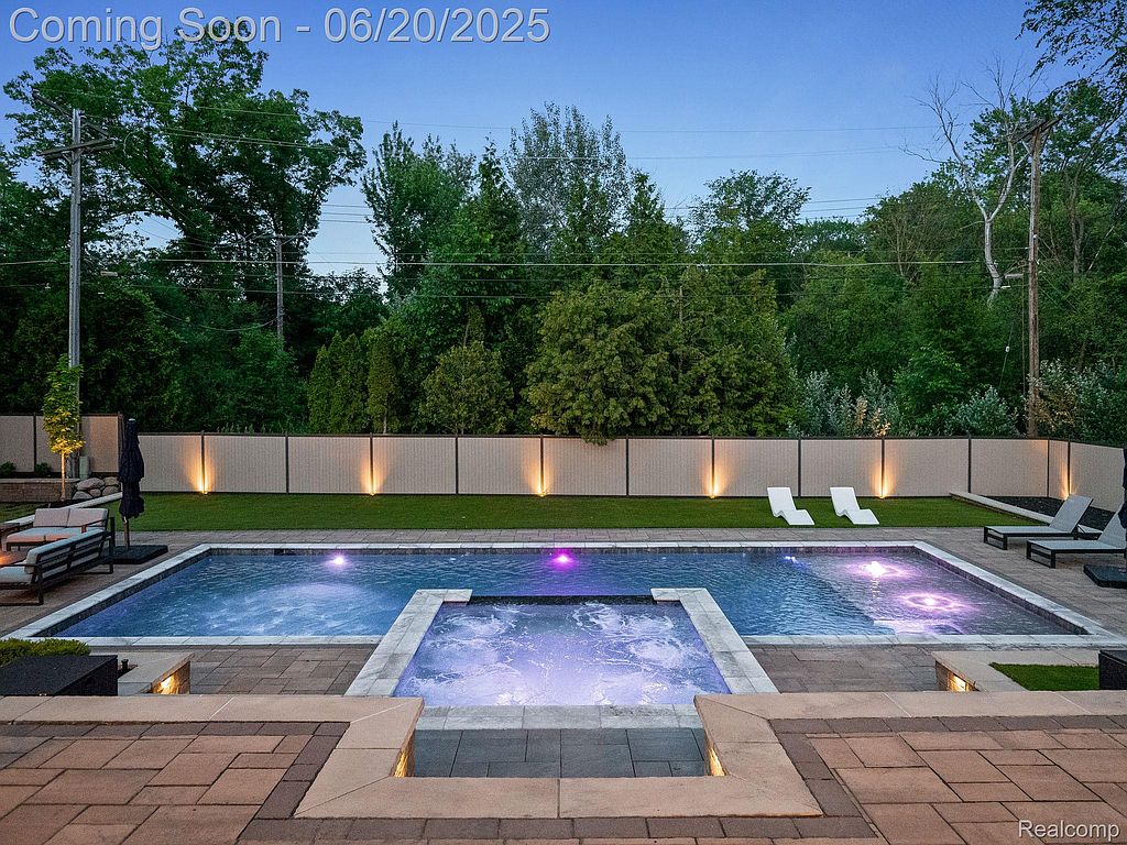 This image showcases a luxurious backyard pool and spa area. The pool features modern lighting and is surrounded by a well-maintained patio and landscaping. Lounge chairs and outdoor seating create an inviting space for relaxation and entertainment.