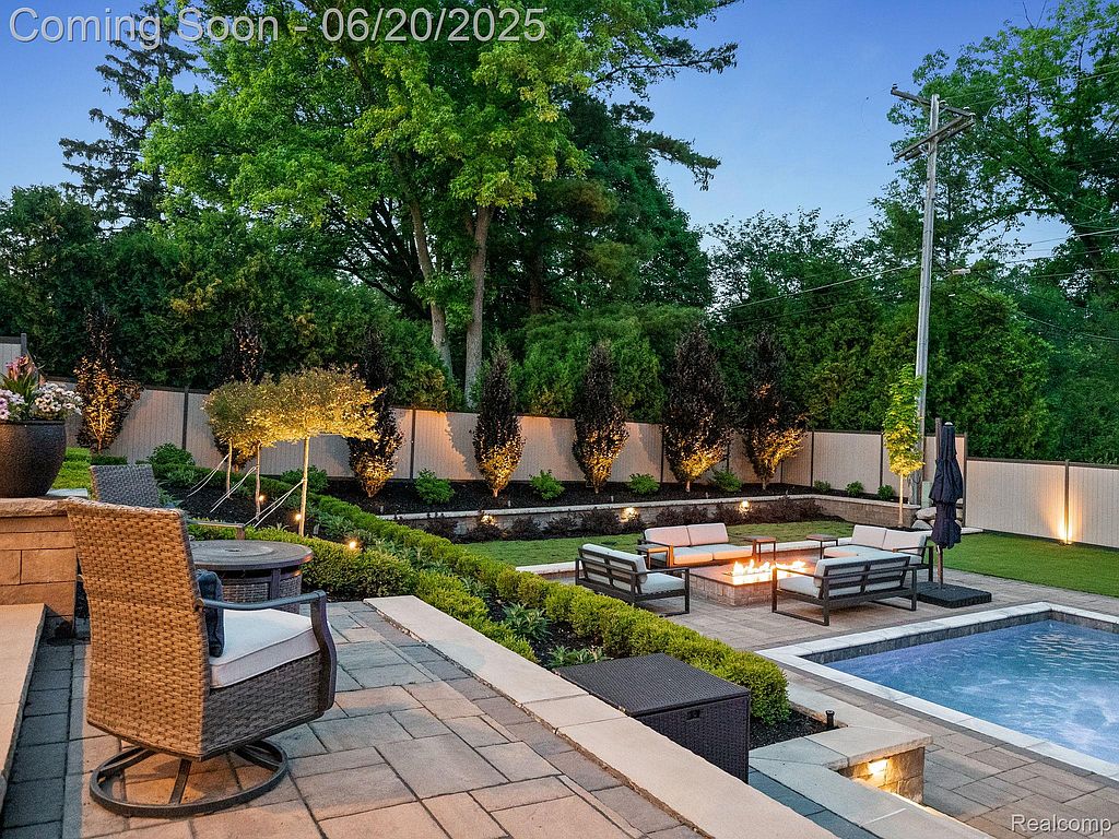 This image showcases a beautifully landscaped backyard featuring a patio with outdoor seating, a fire pit area, and a swimming pool. The garden is well-maintained with lush greenery, decorative lighting, and a privacy fence, creating an inviting and luxurious outdoor living space. The overall impression is one of relaxation and upscale outdoor entertainment.