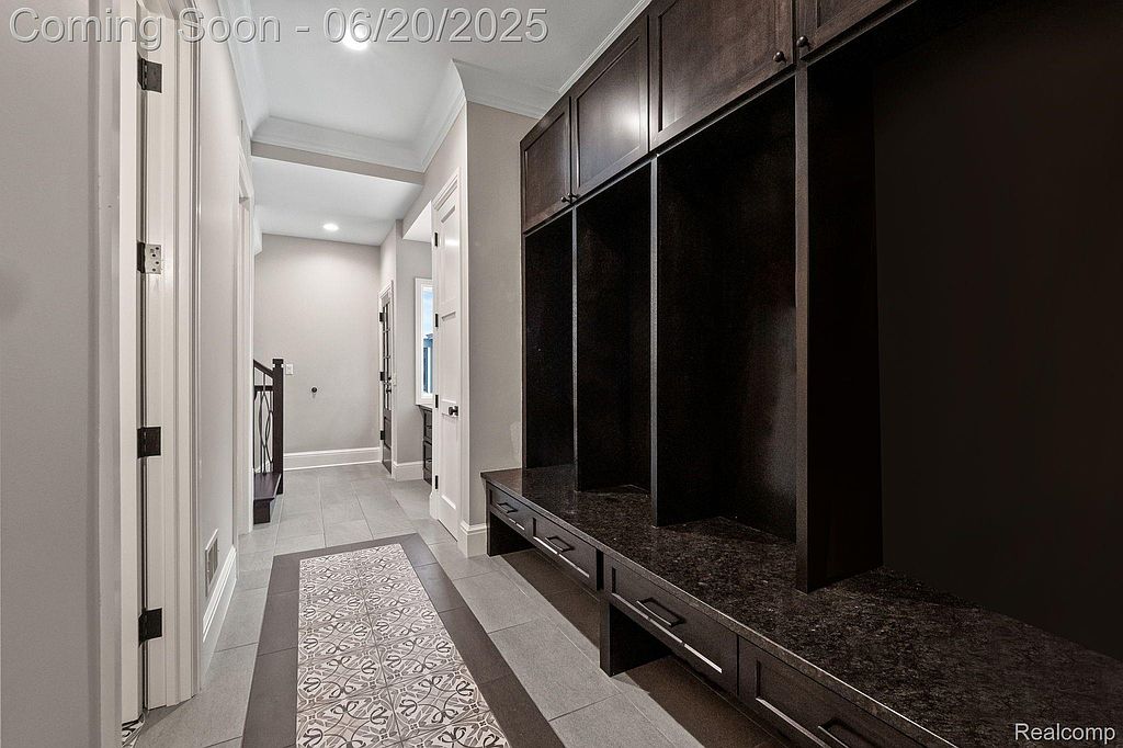 This interior shot showcases a well-lit hallway with a stylish runner rug and a custom built-in storage unit. The dark wood of the storage contrasts with the light gray walls and white trim, creating a modern and sophisticated look. The hallway leads to a staircase with wrought iron railings.