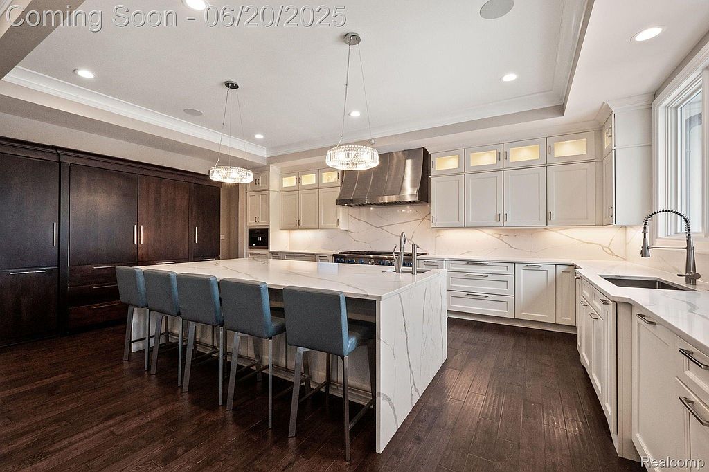 This is a spacious and modern kitchen featuring a large island with seating, white cabinetry, and stainless steel appliances. The kitchen is well-lit with recessed lighting and pendant lights, and the dark wood flooring adds a touch of warmth. The overall impression is one of luxury and functionality.