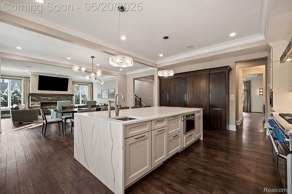 This image showcases a modern, open-concept kitchen with a large island featuring a marble countertop and ample storage. The kitchen seamlessly flows into a living area with a fireplace and dining space, creating an inviting atmosphere. Dark wood flooring and elegant lighting fixtures add a touch of sophistication to the space.