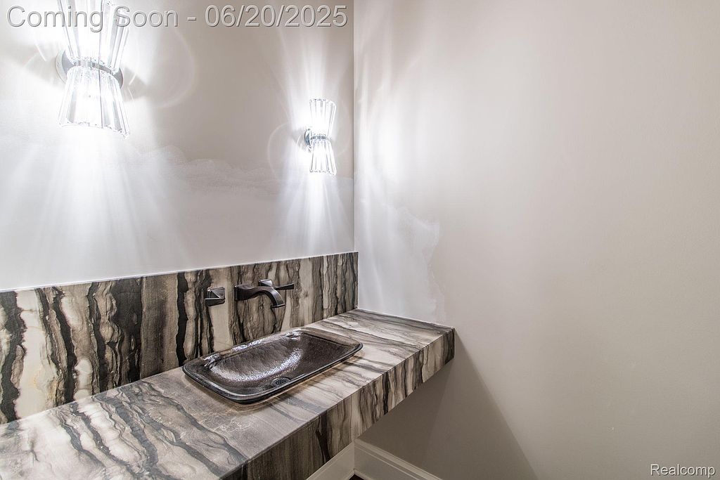 This image showcases a modern guest bathroom featuring a unique marble countertop and backsplash with a dark, rectangular vessel sink. Two decorative sconces provide elegant lighting, highlighting the clean lines and contemporary design. The overall impression is sophisticated and stylish.