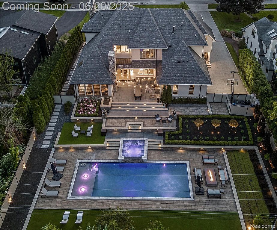 This aerial view showcases a luxurious home with a meticulously landscaped backyard. The property features a large swimming pool with a hot tub, a spacious patio area with outdoor seating and a fire pit, and well-maintained gardens. The overall impression is one of high-end living and outdoor entertainment.