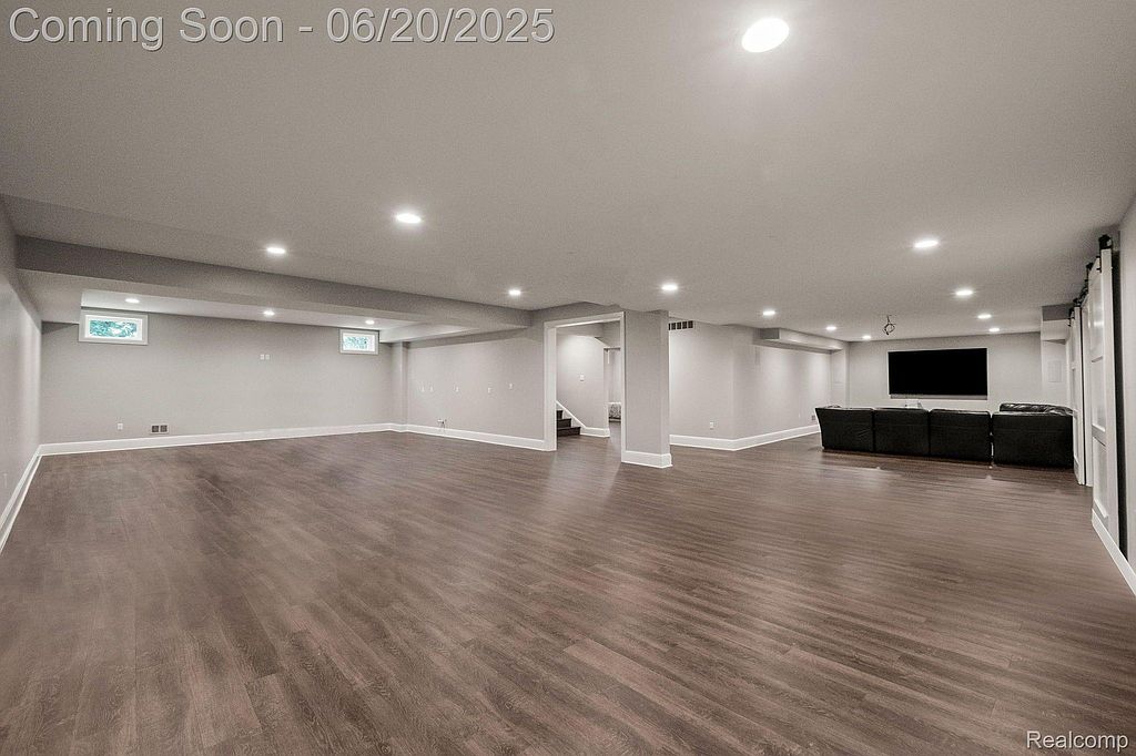 This is a spacious, finished basement featuring modern recessed lighting, neutral paint, and wood-look flooring. The open layout includes a seating area with a large television and a potential recreation or living space. The basement appears clean and well-lit, offering a versatile area for entertainment or relaxation.