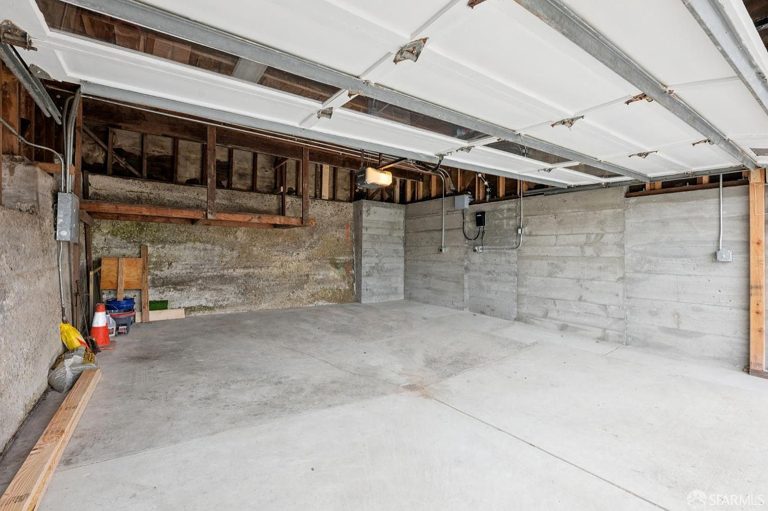 The image showcases an empty garage with a concrete floor and unfinished walls. The garage door is partially open, revealing the support structure and ceiling. The space appears utilitarian and ready for customization, offering potential for storage or a workshop.