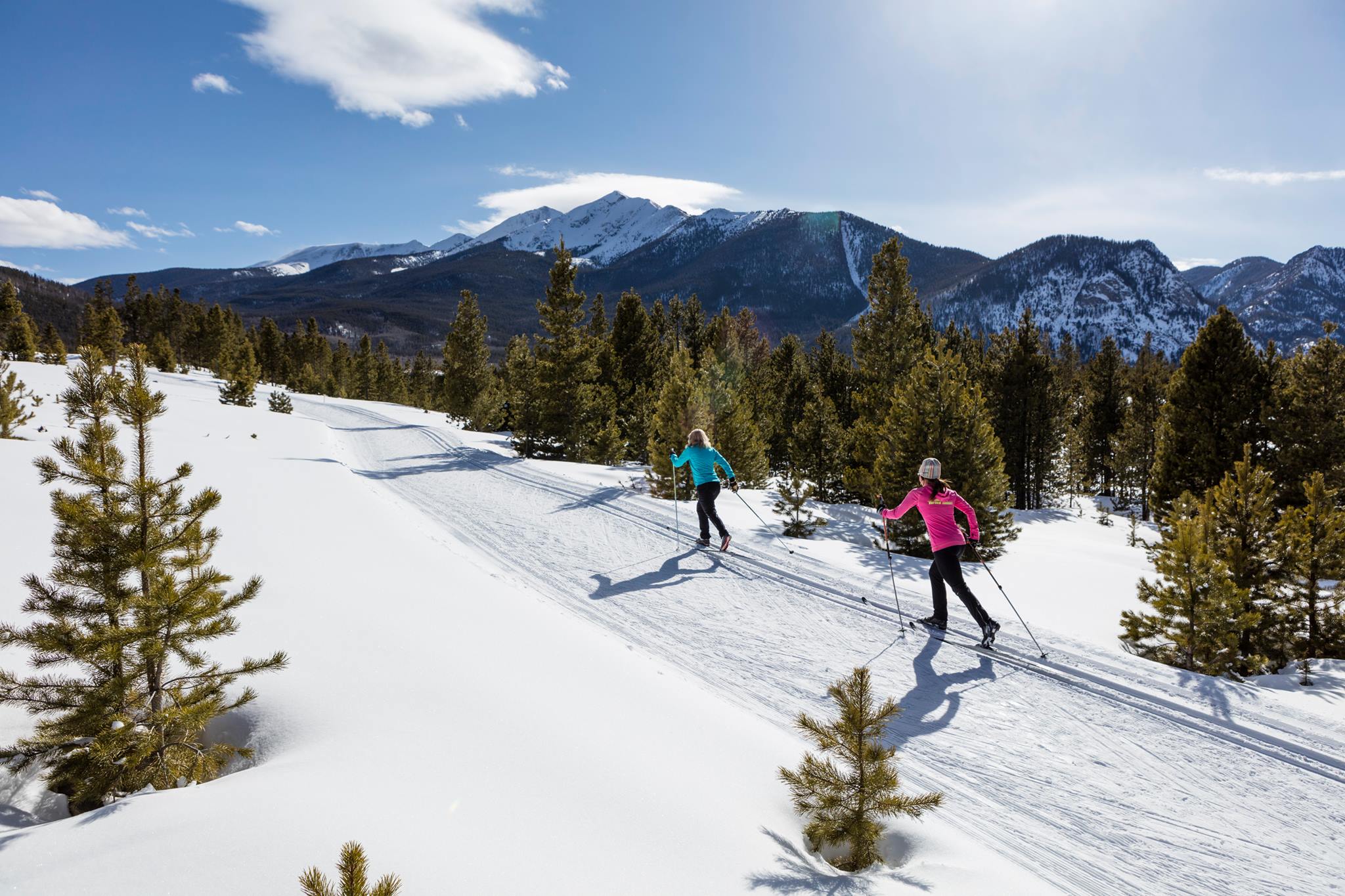 This image highlights a groomed cross-country ski trail set within a scenic, mountainous landscape with dense evergreen forests. The trail serves as a premier outdoor recreational amenity for the community, offering picturesque views and active lifestyle opportunities in a high-altitude, snowy mountain environment.