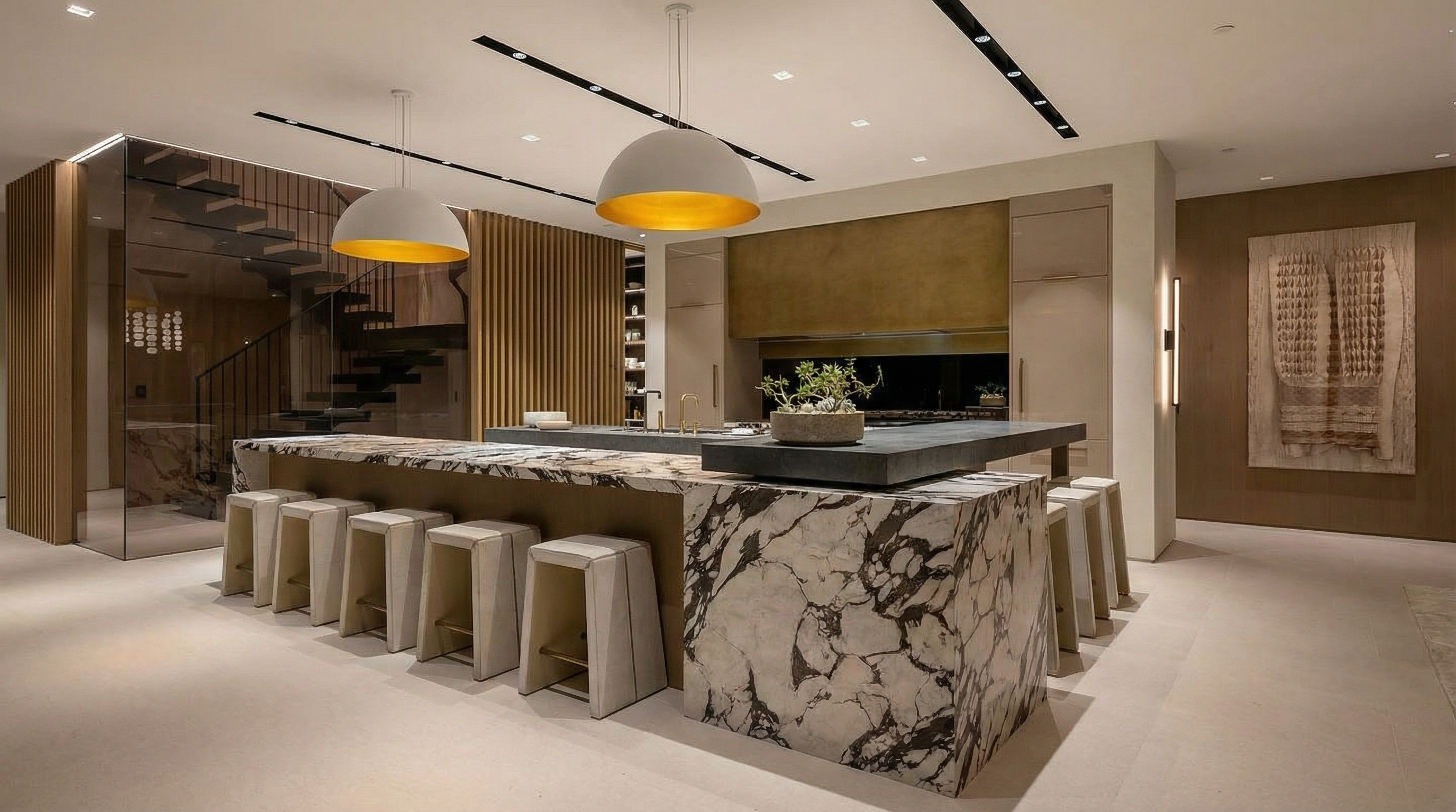 This image showcases a modern, high-end kitchen featuring a marble island with bar seating. The kitchen is illuminated by two large pendant lights and linear track lighting, creating a warm and inviting ambiance. The design incorporates sleek cabinetry and countertops, suggesting a luxurious and functional space perfect for cooking and entertaining.