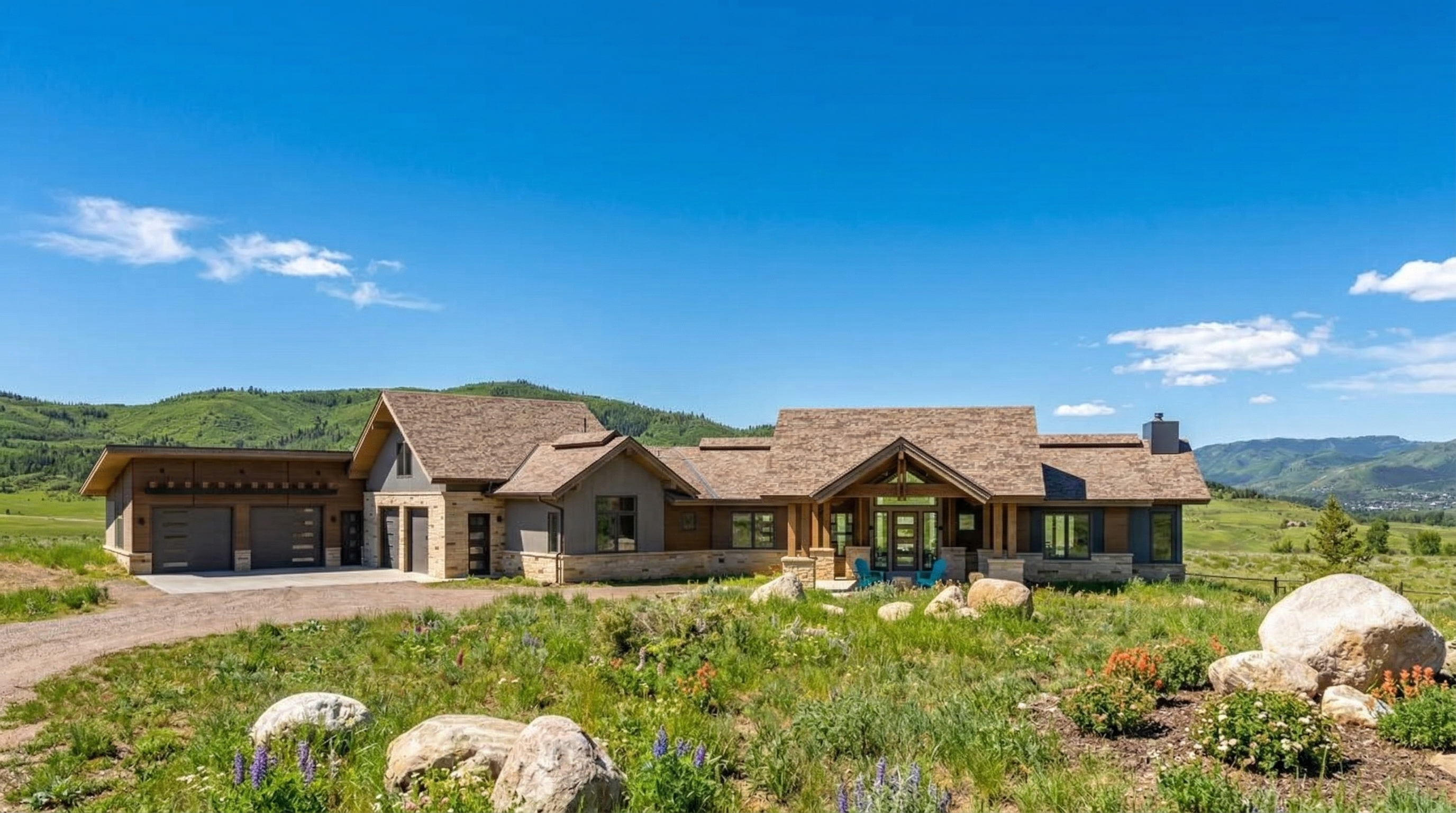 This stunning mountain-style home features a blend of natural stone and wood siding, perfectly integrated into the surrounding landscape. The architectural design includes an expansive multi-car garage, a stately covered entryway, and large windows that invite abundant natural light. The property offers a serene and picturesque setting with impressive views of the rolling hills.