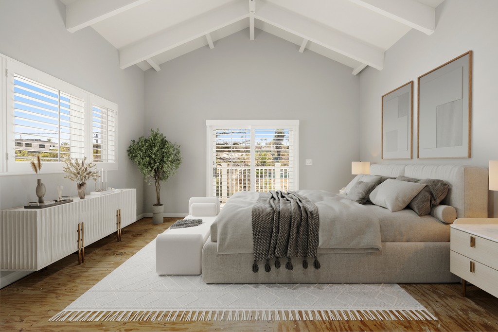 This bright and airy primary bedroom features a vaulted ceiling with exposed beams and a neutral color palette. A plush, upholstered bed serves as the focal point, complemented by a textured area rug, a sleek white sideboard, and a potted tree that adds a touch of greenery. Large windows with plantation shutters allow for natural light, creating a serene and inviting atmosphere.