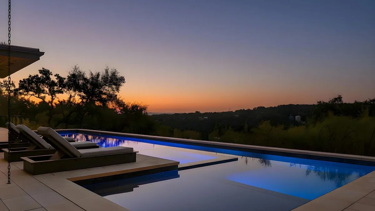 This image showcases a stunning infinity pool at dusk, reflecting the colorful sky. Deck chairs are positioned by the pool, offering a relaxing space with panoramic views. The pool's design and location maximize the property's appeal, creating an inviting outdoor oasis.