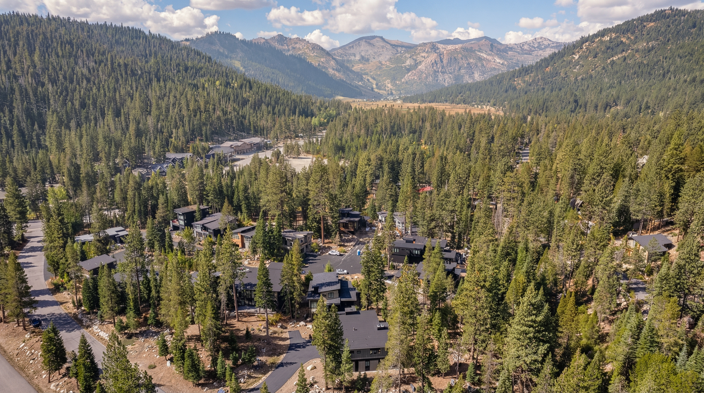 This aerial view showcases a neighborhood nestled within a dense forest, leading to distant mountains. Modern homes with dark roofs are visible amidst the trees, blending with the natural surroundings. The image emphasizes the property's location within a scenic and serene environment.