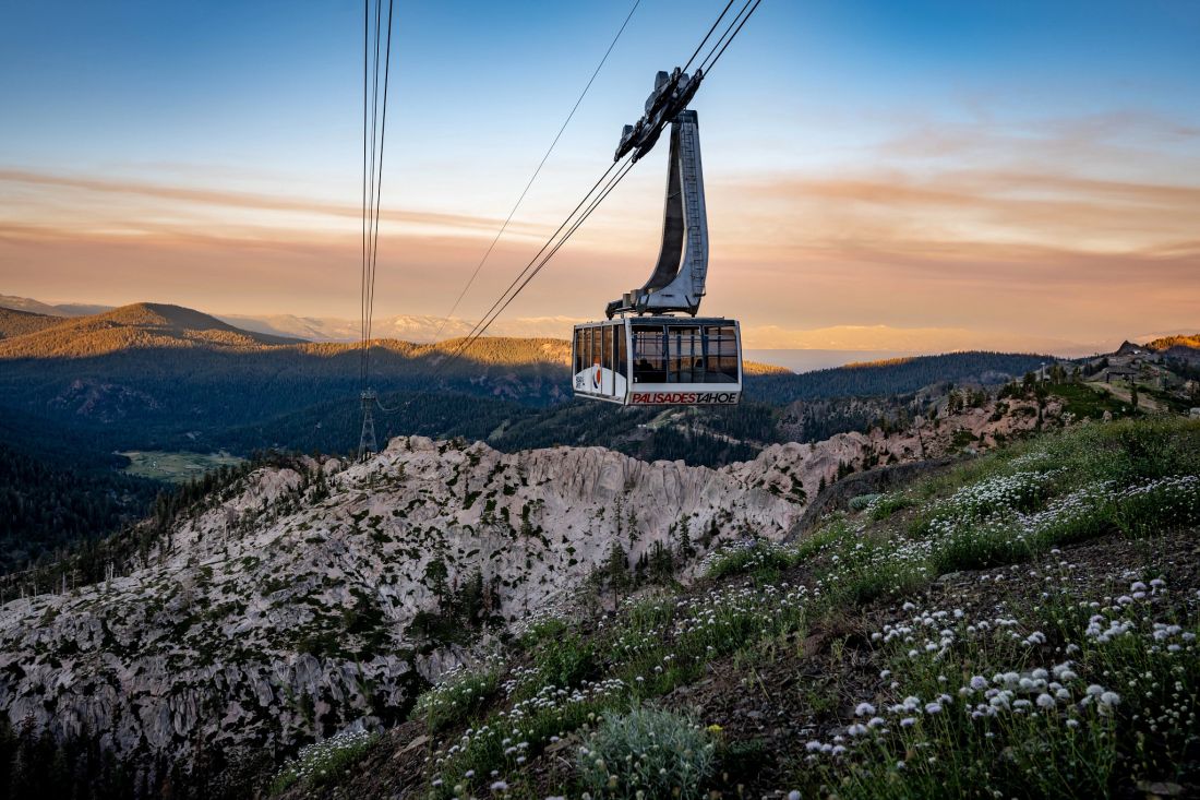 This aerial shot showcases a gondola ascending towards a mountain peak, highlighting the stunning natural surroundings and recreational opportunities. The landscape features rocky terrain, vibrant greenery, and distant mountain ranges, indicating a premium location for those who appreciate nature and outdoor activities. The presence of the gondola suggests easy access to higher elevations and panoramic views, making this a potentially desirable property feature.