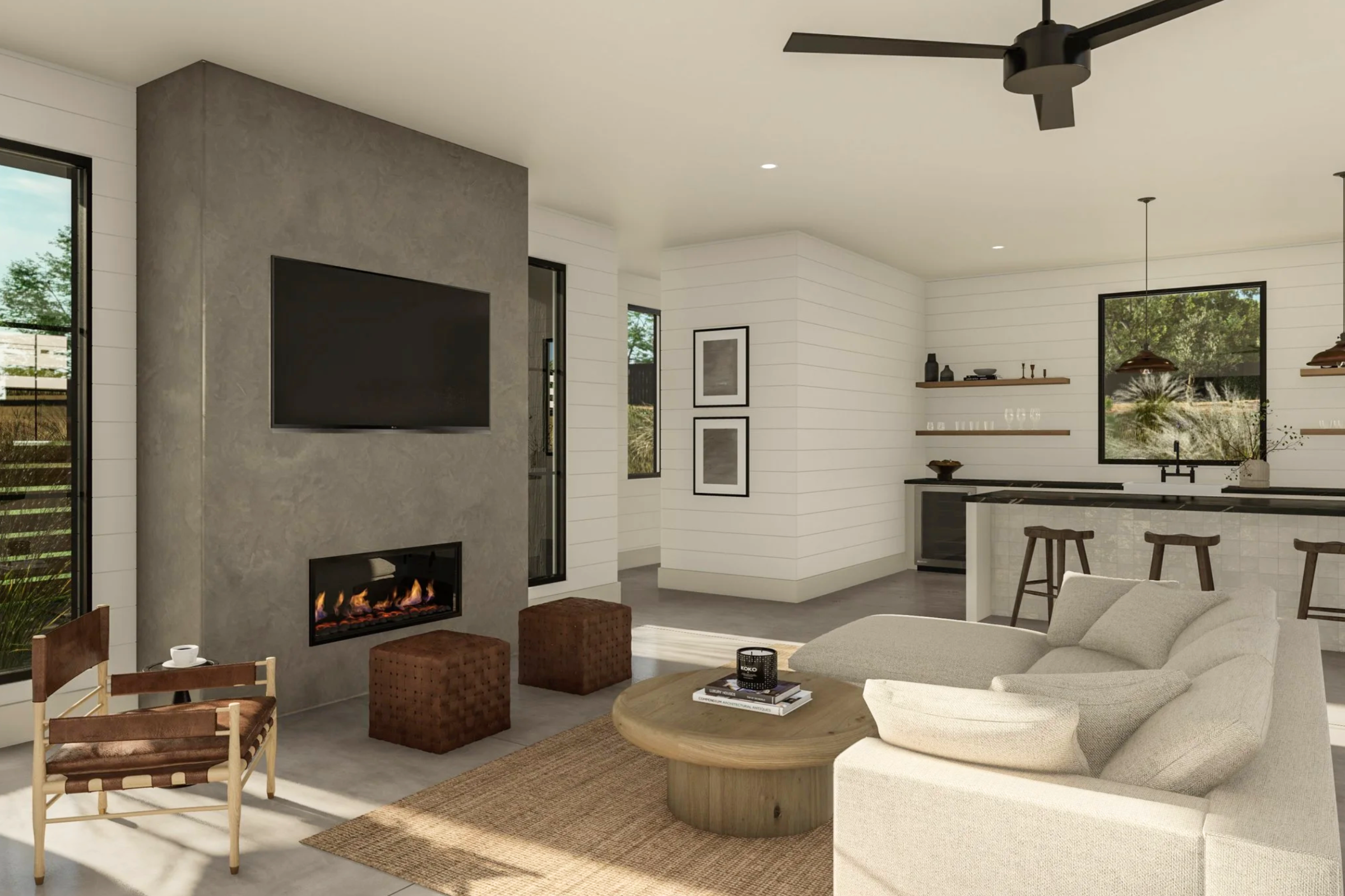 This modern open-concept living space features a striking concrete-textured fireplace wall with a linear fireplace and wall-mounted television. The room exudes comfort with a neutral-toned sectional sofa, a natural fiber area rug, and a leather accent chair, seamlessly flowing into a bright kitchen area with bar seating. The design emphasizes a warm, minimalist aesthetic with clean lines and high-quality finishes, perfect for contemporary living.
