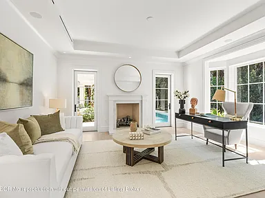 The image showcases a bright and elegant home office. It features a white sofa, a round coffee table, and a dark-colored desk with a gray chair. The room is well-lit with natural light from a bay window and includes a fireplace centered between French doors, lending a sophisticated and inviting atmosphere suitable for a professional working space.