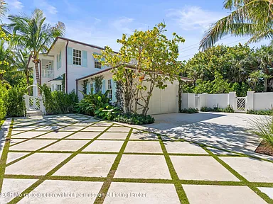 This is a front exterior view of a two-story home featuring a well-manicured lawn and a paved driveway with grass inlays. The house has white siding with blue shutters and noticeable landscaping. An attached garage is partially visible on the right side.