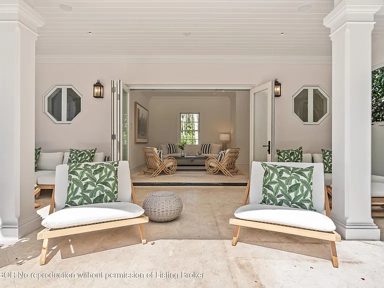 This image depicts a covered patio area with comfortable seating, seamlessly blending indoor and outdoor living. The open doors lead to an interior space, suggesting a cohesive design, while stylish furniture and architectural details like the windows and prominent columns enhance the space's appeal. The neutral color palette creates a relaxing and sophisticated atmosphere.