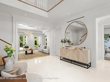 This image showcases a bright and spacious entryway featuring high ceilings and a grand staircase. The area is decorated with modern furniture including a console table and a round mirror, creating a welcoming and stylish ambiance. The flooring appears to be white tile, enhancing the light and airy feel of the space.