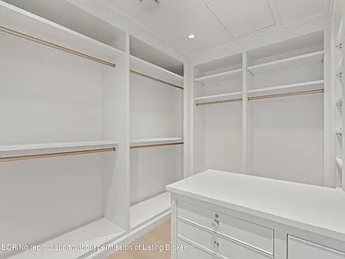 This image showcases a well-organized walk-in closet with white shelving and hanging rods. The closet features ample storage space, indicating a generous area for clothing and accessories. The clean, bright design is appealing and suggests luxury organization.