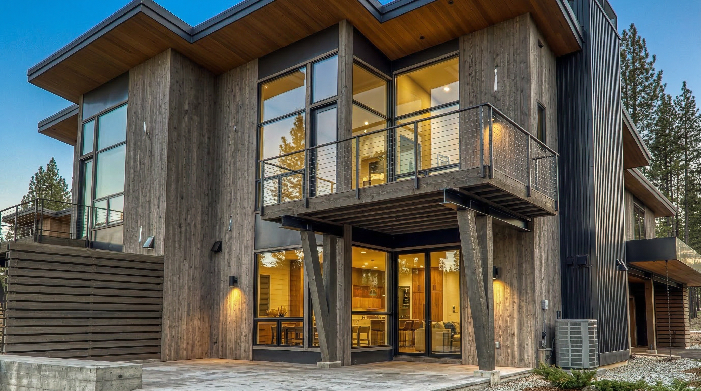 This is a contemporary home featuring a blend of wood and metal exterior elements. The design incorporates large windows providing ample natural light and an inviting balcony area. The landscaping is minimal, emphasizing the modern aesthetic of the property.