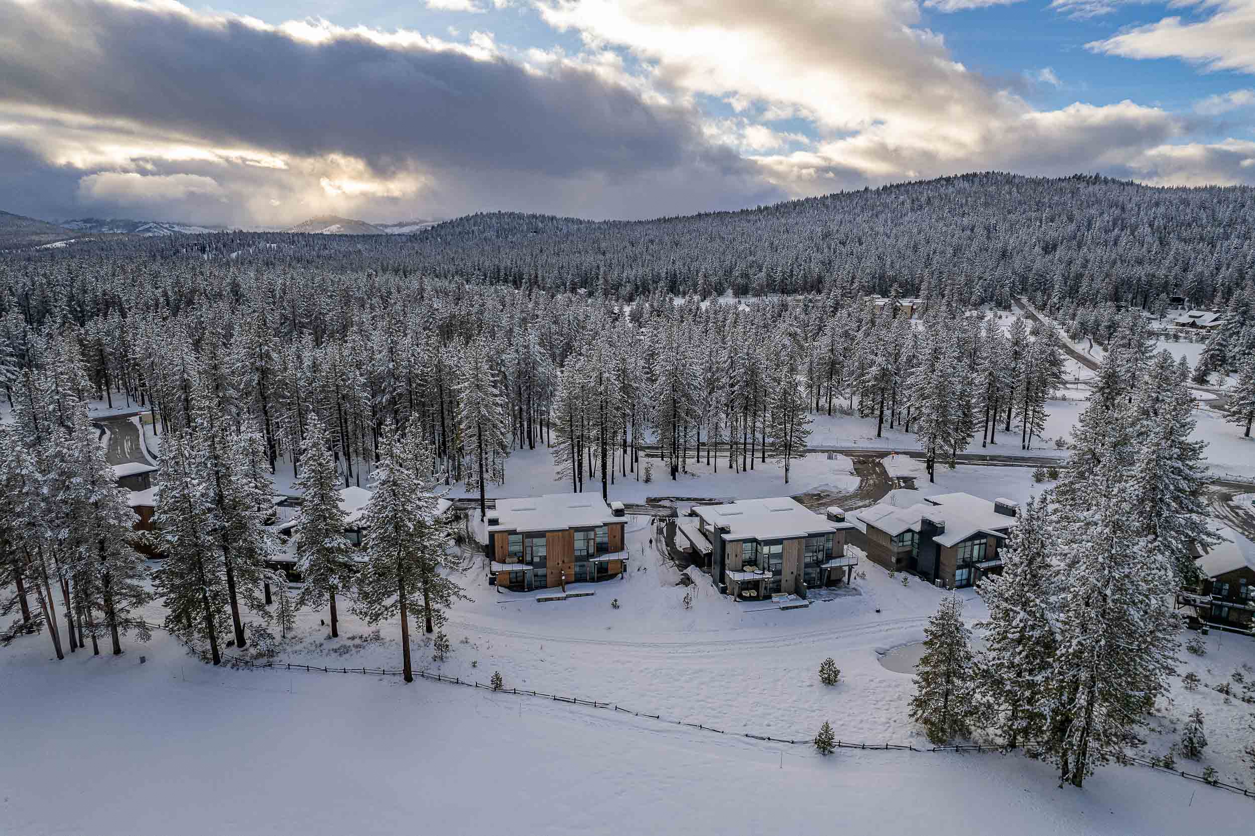 This aerial view showcases a set of modern homes nestled in a snow-covered, wooded area. The homes feature contemporary architectural designs with clean lines and neutral exterior colors. The surrounding landscape is heavily wooded, creating a sense of privacy and seclusion, making this a desirable location for buyers seeking a serene retreat.