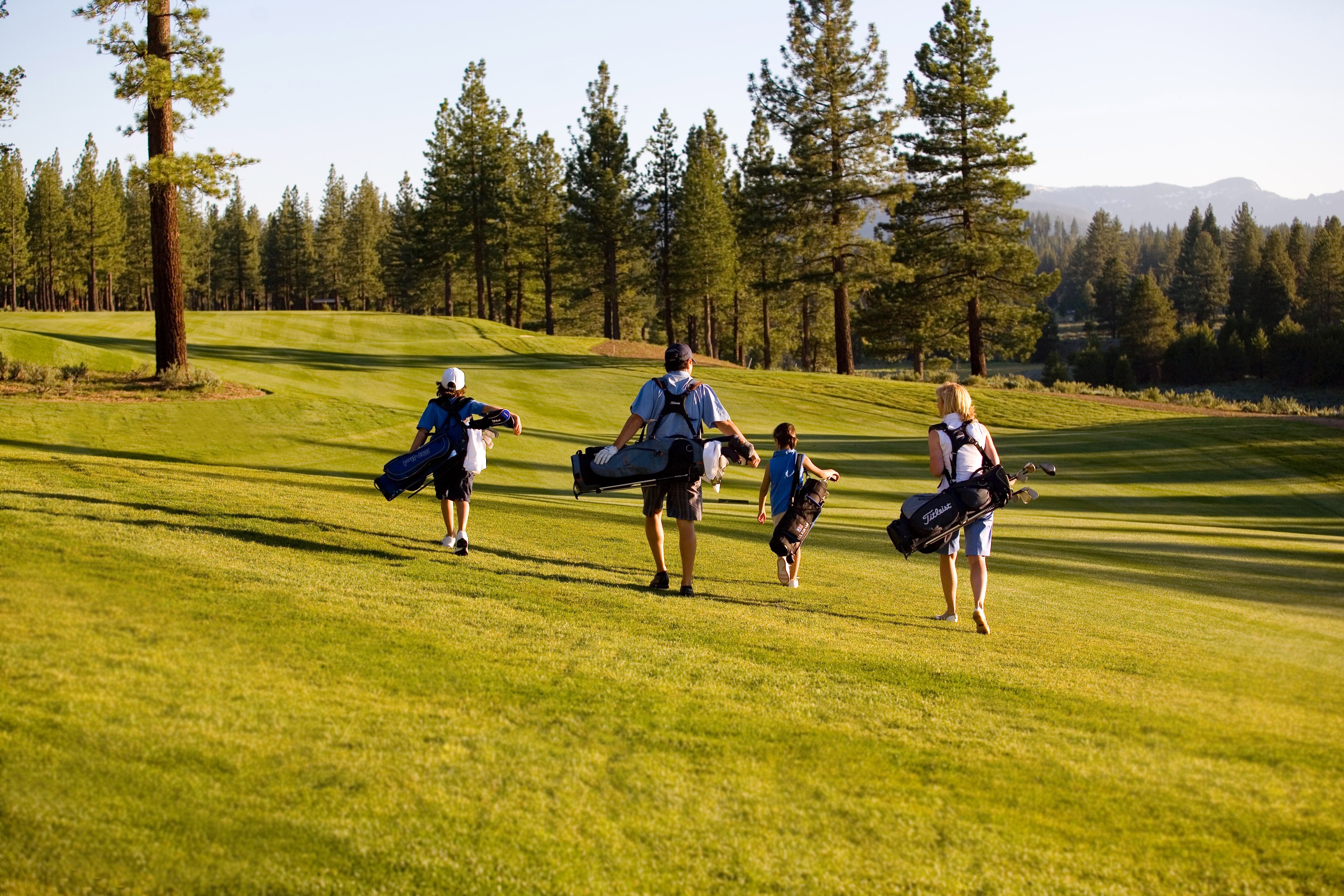 This exterior shot showcases a well-maintained golf course with lush green grass. A family is seen walking across the green, carrying golf bags. The scene suggests an active and luxurious lifestyle, perfect for golf enthusiasts.
