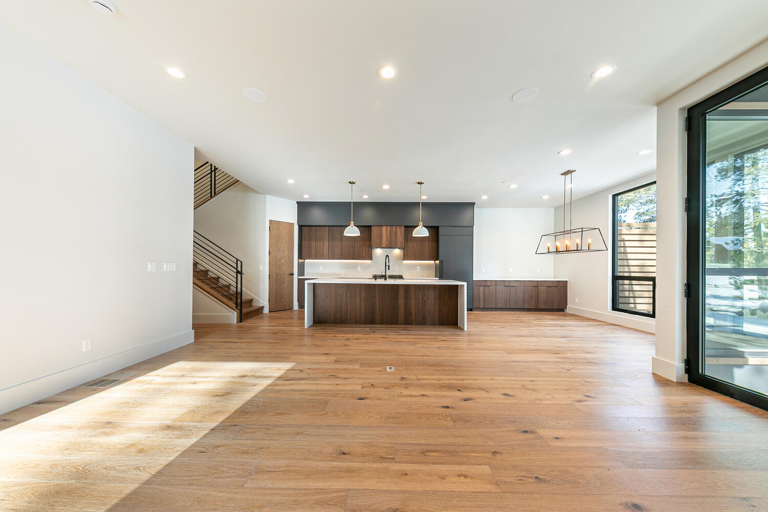 This is a spacious, modern kitchen and living area. The kitchen features dark wood cabinetry with a contrasting white countertop island. Natural light floods the space, highlighting the hardwood floors and open floor plan, suggesting a contemporary and inviting home.