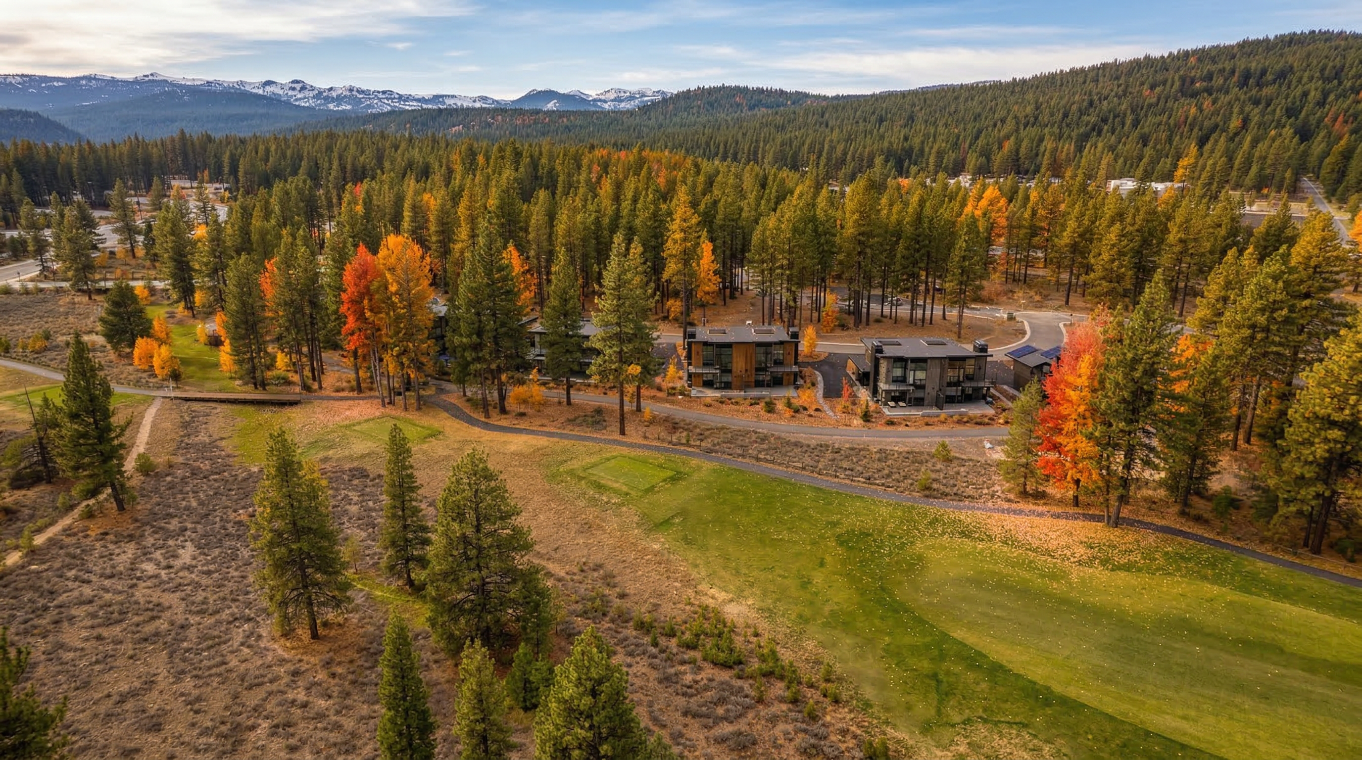 This aerial shot showcases a luxury residential property nestled within a wooded landscape with vibrant fall foliage. The buildings feature modern design and are set back from a golf course. The setting offers a blend of natural beauty and upscale living appealing to potential buyers seeking a serene yet sophisticated environment.