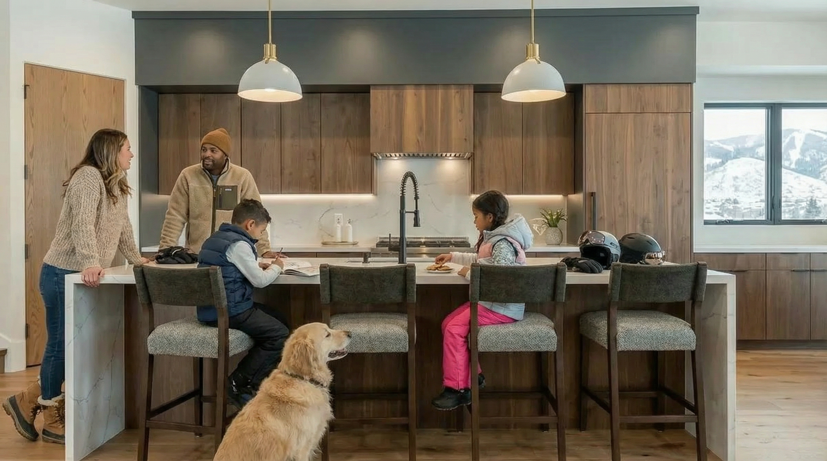 This inviting kitchen features walnut cabinetry contrasted with white countertops and sleek, modern pendant lighting. A large island anchors the space, providing seating for a family gathered around. The open layout and view to the outdoors create a warm and welcoming atmosphere, perfect for both everyday living and entertaining.