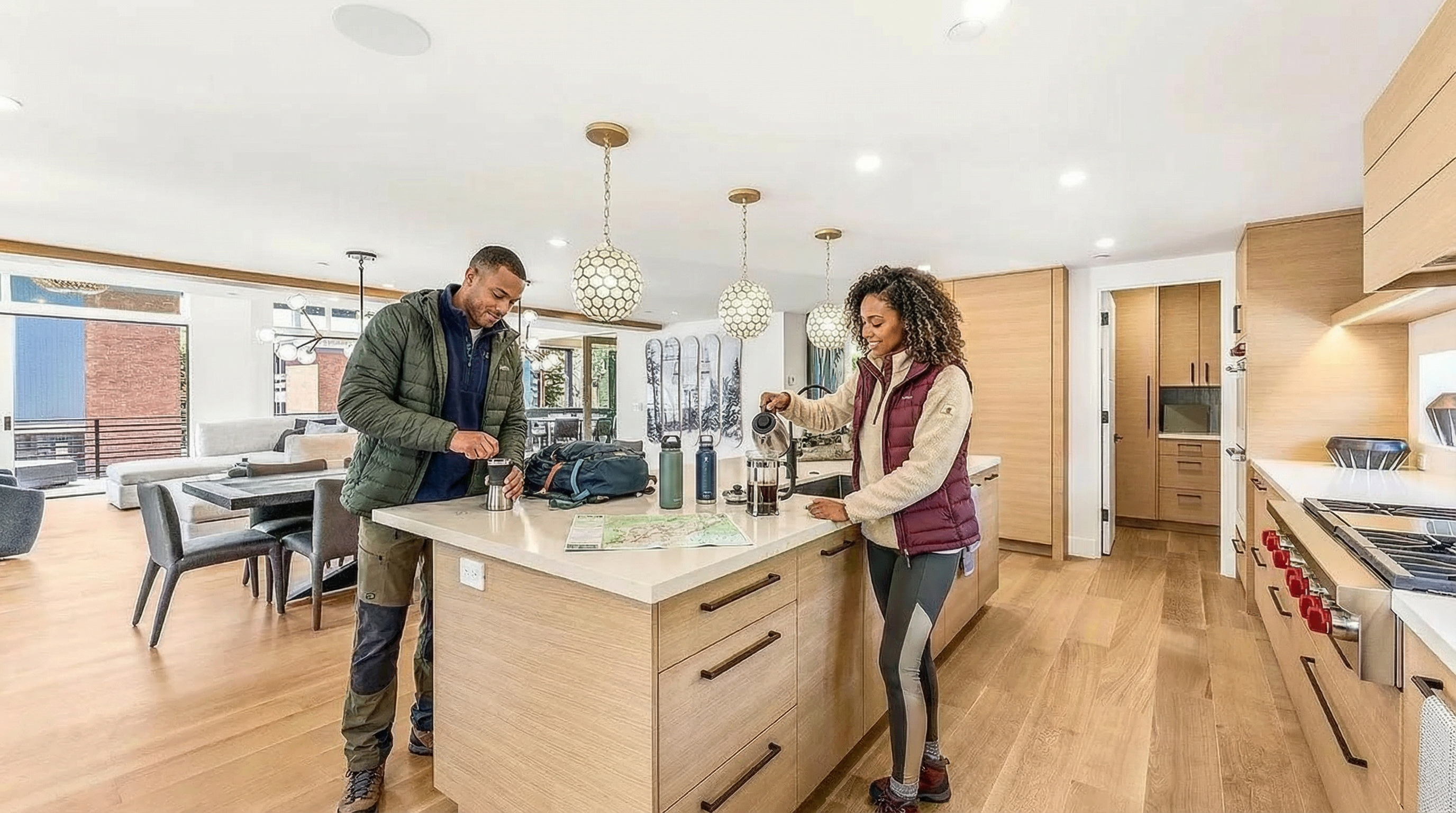 This is an interior shot showcasing a modern kitchen. The kitchen island serves as a focal point with contemporary lighting fixtures hanging above. The image highlights the open-concept design, which flows into a living and dining area, demonstrating the home's functional layout and inviting space.