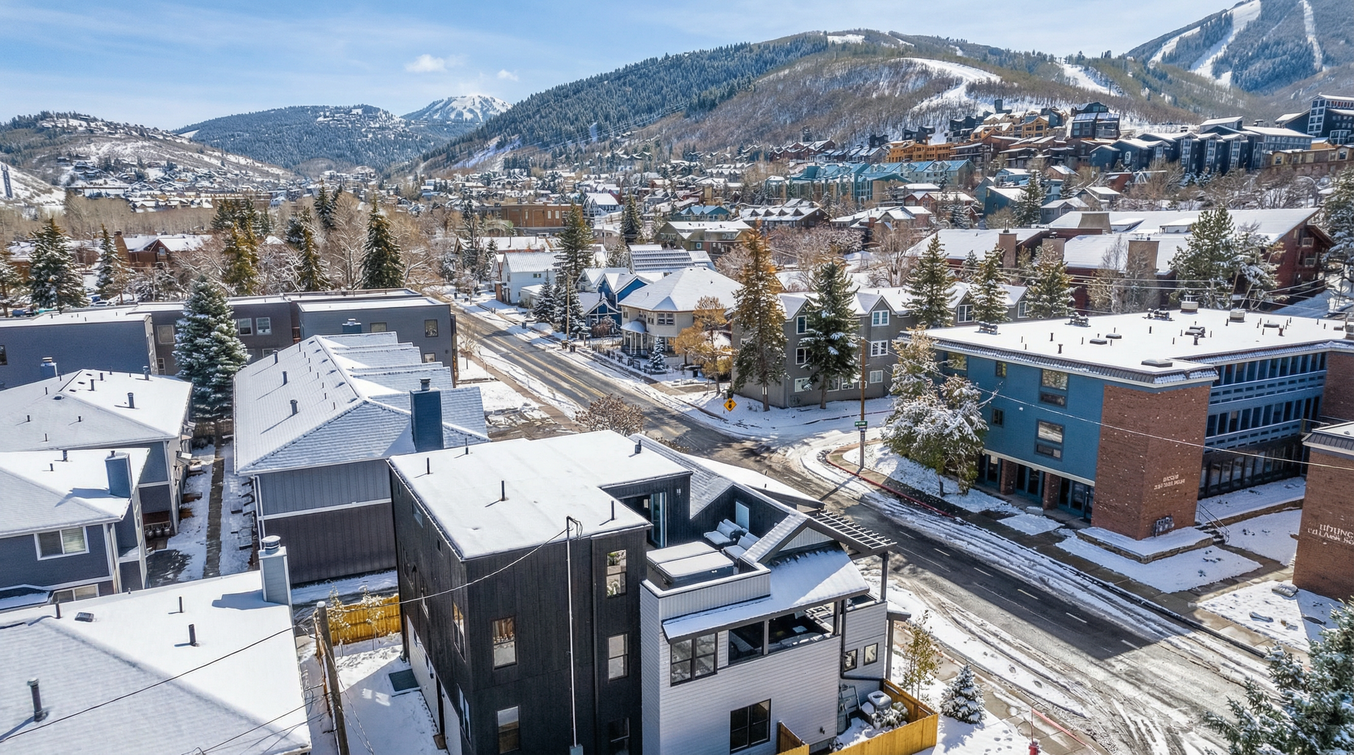 This aerial view presents a charming mountain town blanketed in snow, showcasing a mix of residential buildings. The architecture is consistent with mountain resort style, featuring a variety of roof lines. The snowy landscape enhances the picturesque charm, making it appealing for potential buyers seeking a tranquil mountain escape.
