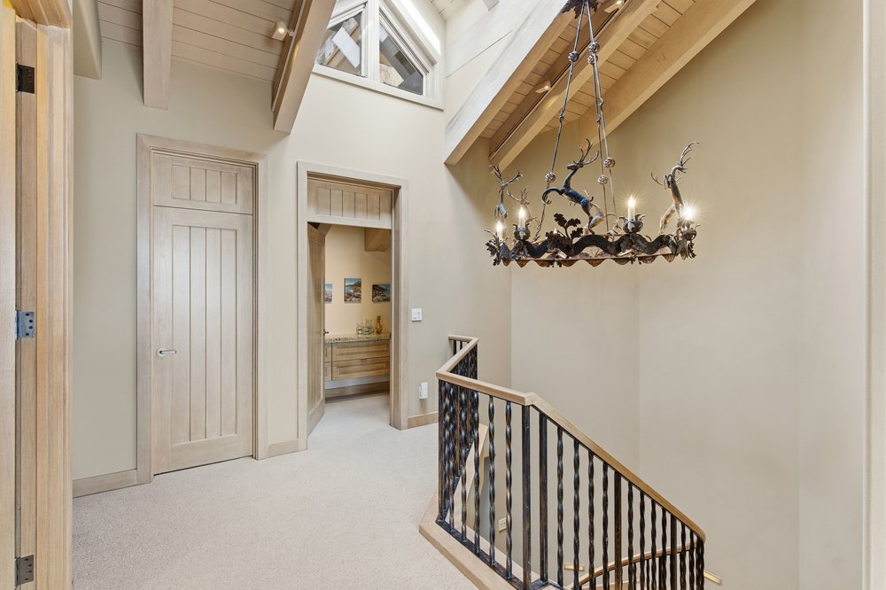 This interior shot showcases a hallway with stairs, featuring a unique chandelier with deer figures. The walls are painted in a neutral tone, complementing the light-colored wooden doors and trim. The staircase has a wrought iron railing with wooden accents, adding a touch of rustic elegance to the space.